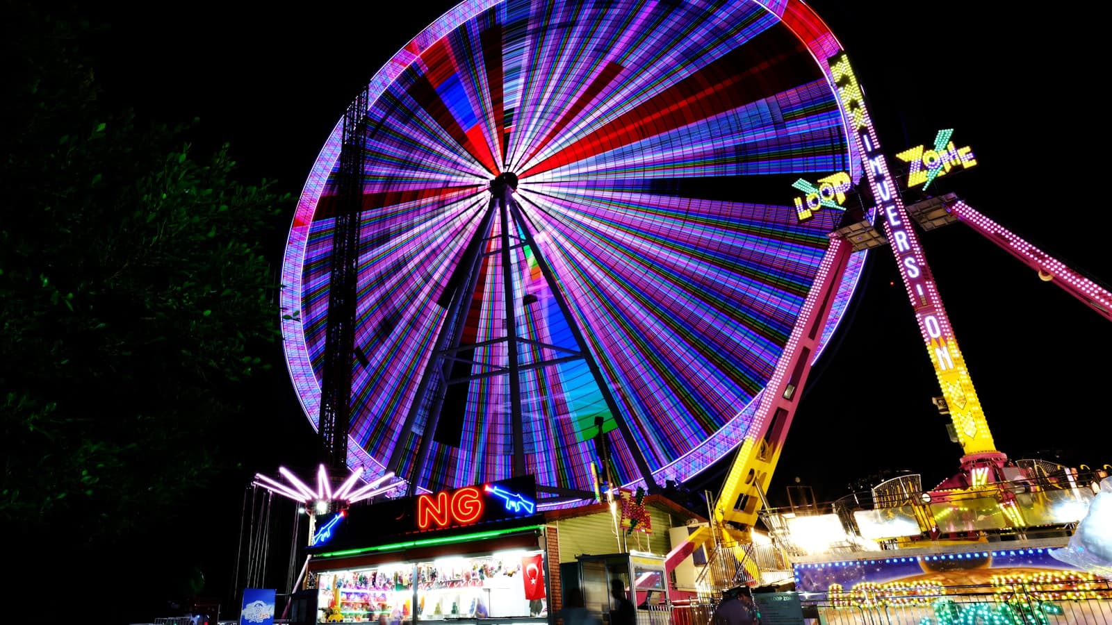 A colorful Ferris wheel and carnival rides at night